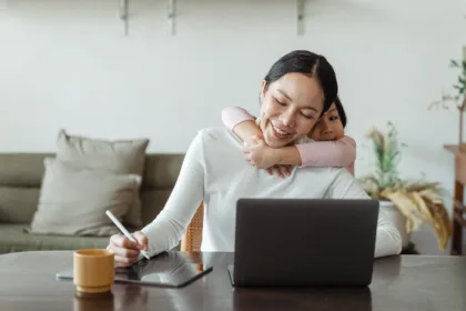 Young girl hugging her mother who is sitting at a desk working on care proceedings